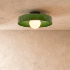 Clérachic shallow green glass disc ceiling light with an opal globe bulb, lit, set against a limewash plaster wall.