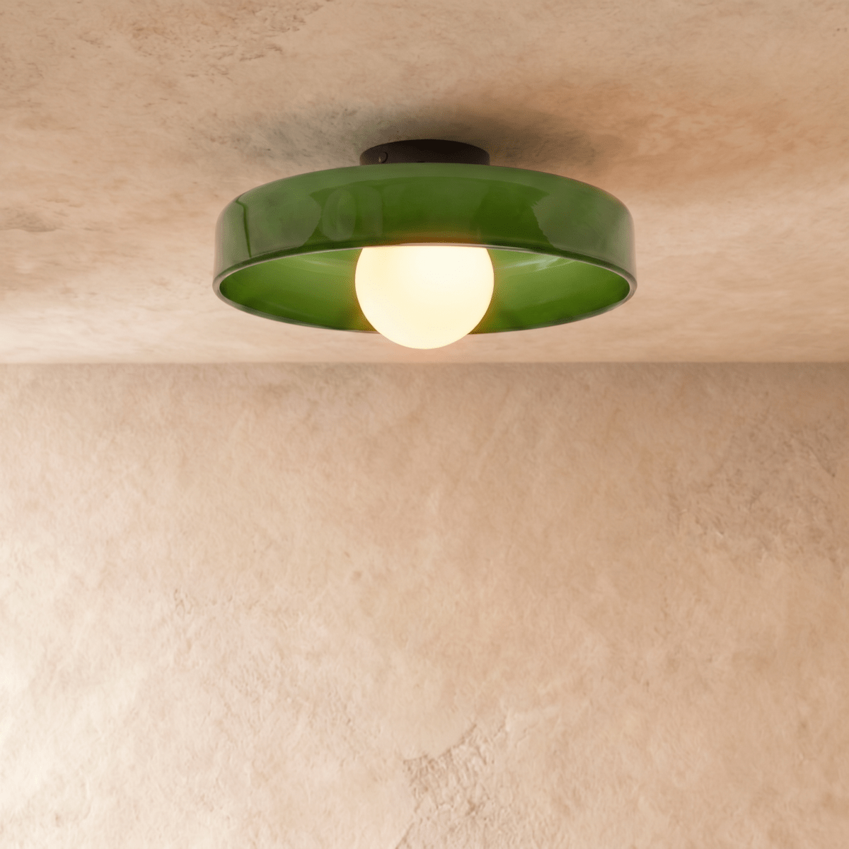 Clérachic shallow green glass disc ceiling light with an opal globe bulb, lit, set against a limewash plaster wall.