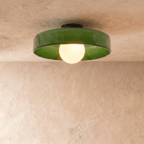 Clérachic larger green glass disc ceiling light with a glowing opal globe bulb and black canopy on plaster.