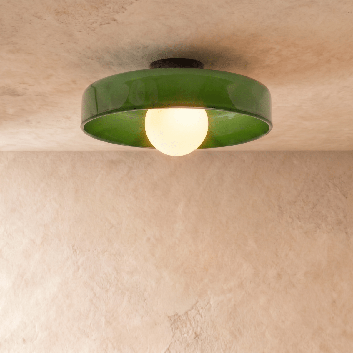Clérachic larger green glass disc ceiling light with a glowing opal globe bulb and black canopy on plaster.