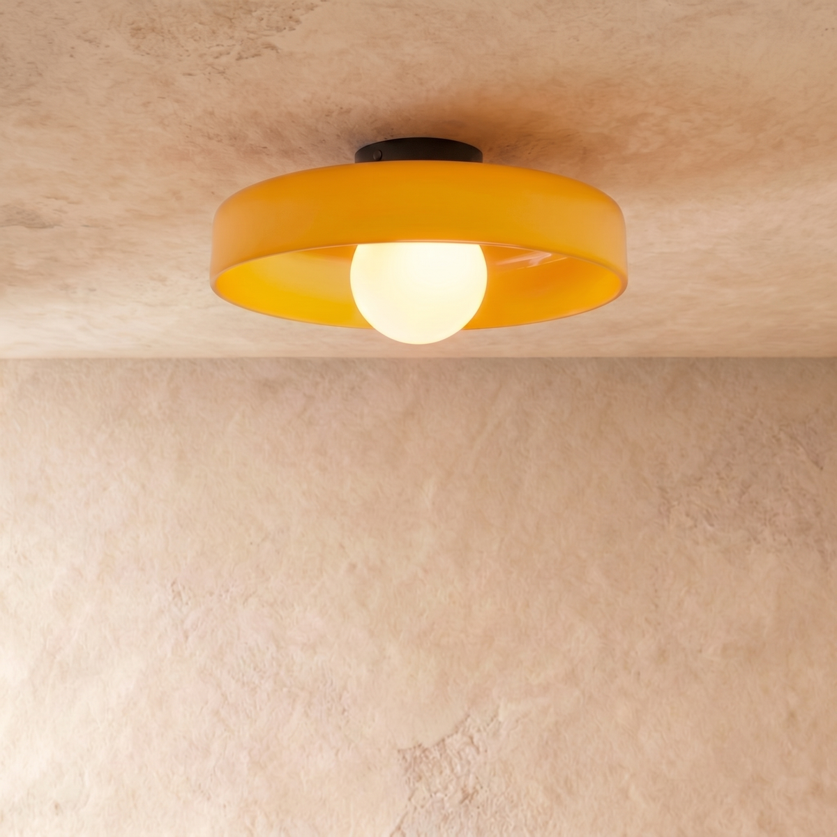Clérachic shallow orange glass disc ceiling light with an opal globe bulb, lit, against a limewash plaster wall.