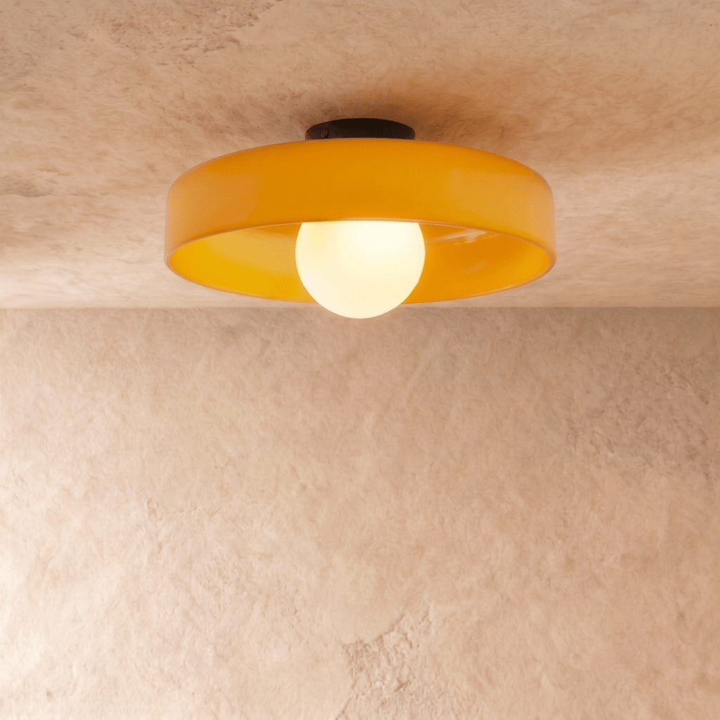 Clérachic larger orange glass disc ceiling light with a glowing opal globe bulb and black canopy on plaster.