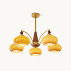 Five caramel glass shades on curved gold arms around a walnut-toned wooden centre column, on this Clérachic chandelier, shown on a plain white backdrop.