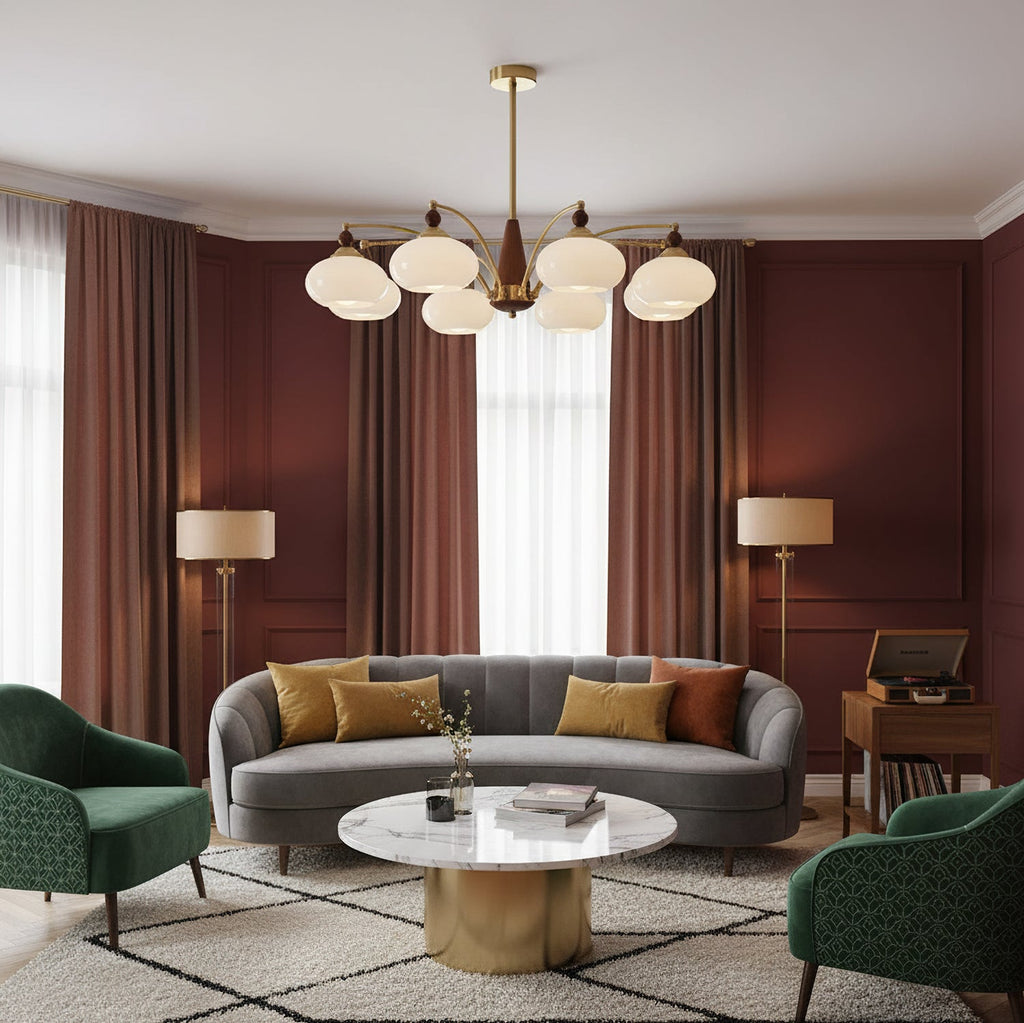 A Clérachic chandelier with white glass shades hangs in a living room with brick-red curtains, a grey curved sofa and a round marble table.