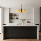 Caramel glass Clérachic chandelier hanging over a kitchen island with a speckled stone top, in a bright white kitchen.