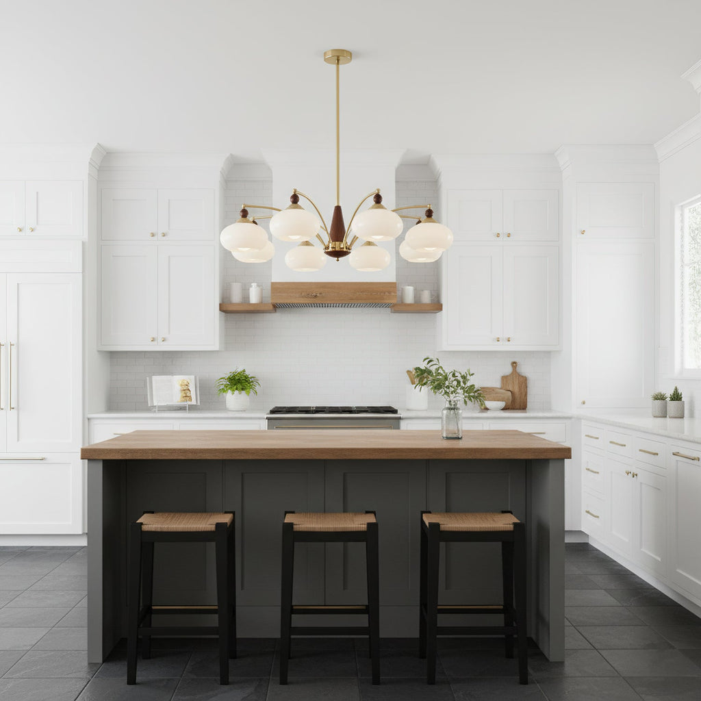 White glass Clérachic chandelier above a kitchen island with a wood top and three rattan stools, in a white shaker-style kitchen.