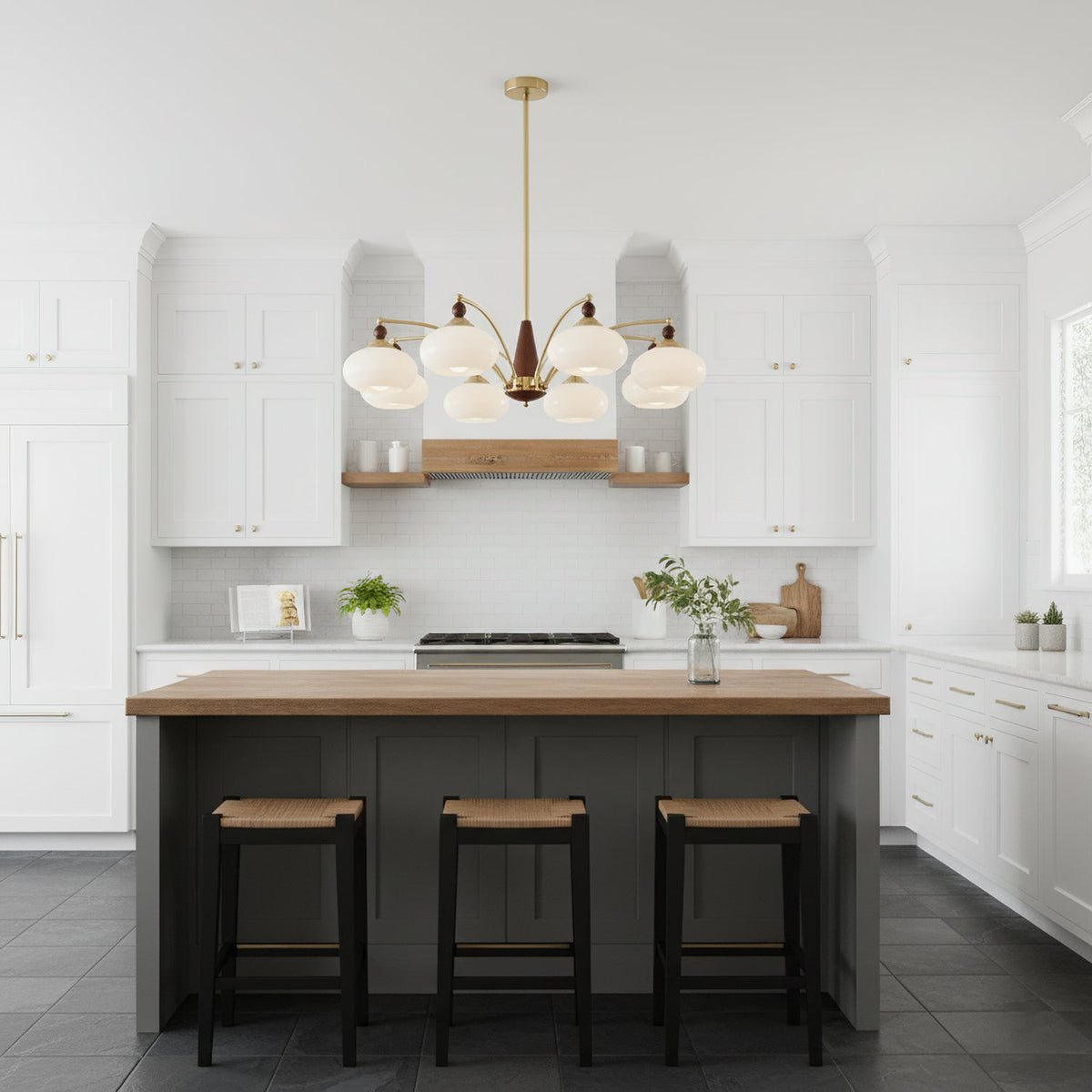 White glass Clérachic chandelier above a kitchen island with a wood top and three rattan stools, in a white shaker-style kitchen.