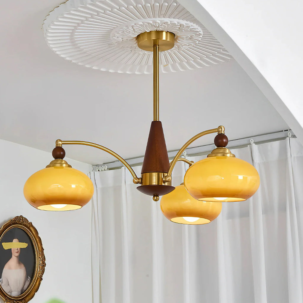 Looking up at a three-head Clérachic chandelier with caramel glass shades, hanging below a pleated white ceiling rose.