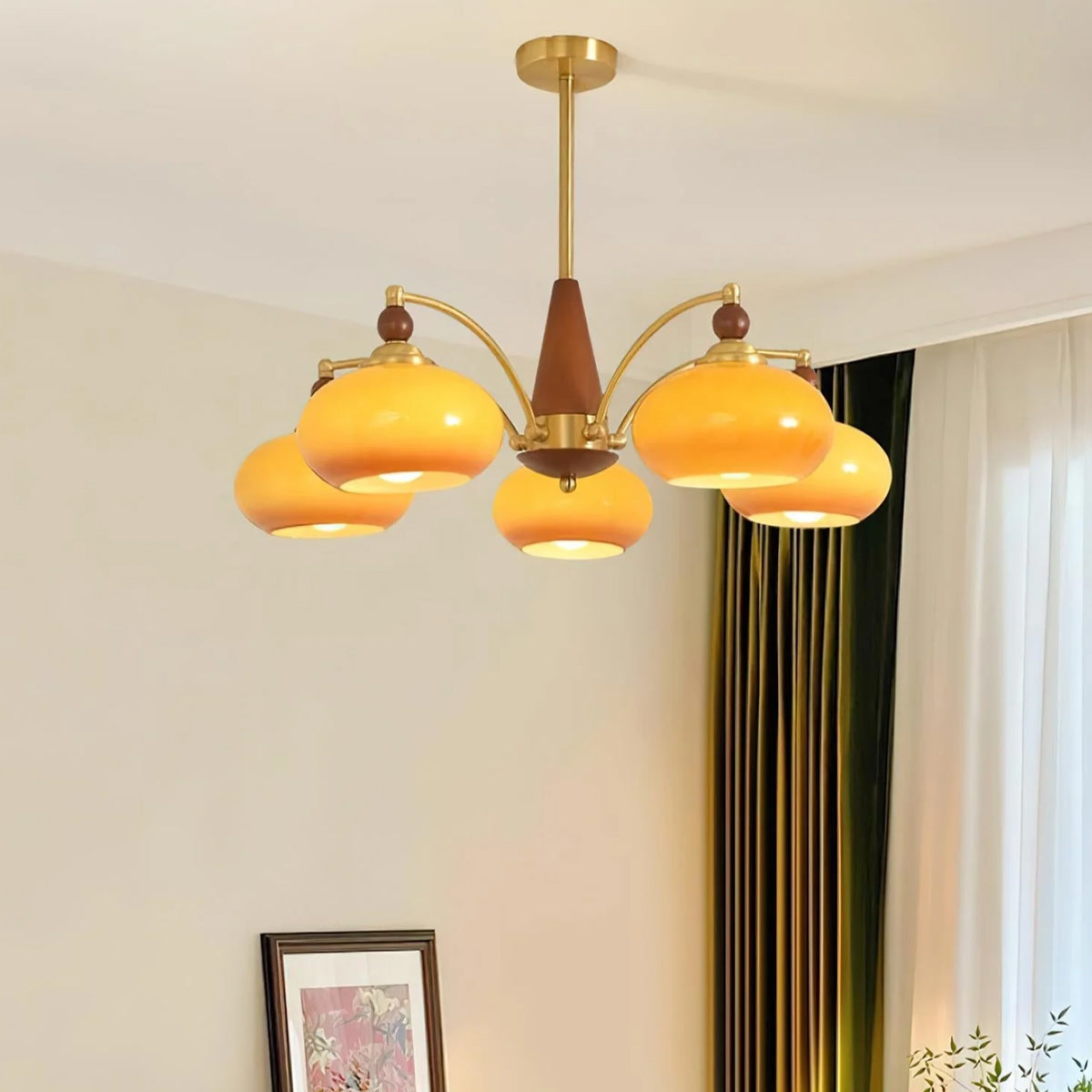 This Clérachic chandelier with caramel glass shades hangs in a cream room with green curtains and a framed print in the corner.