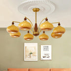 Eight caramel glass shades spread on gold arms from this Clérachic chandelier, hung against a sage green wall with framed posters.