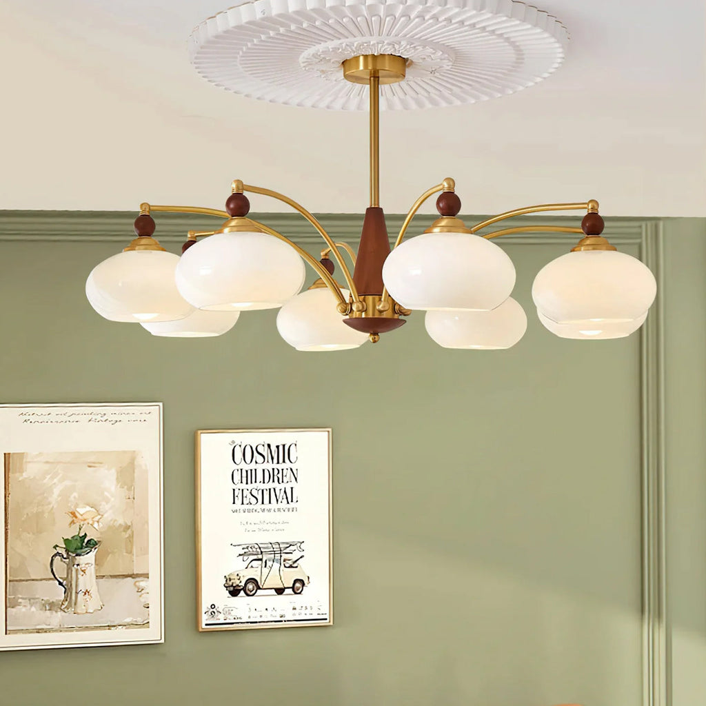This Clérachic chandelier with eight white glass shades hangs against a sage green wall, above two framed posters.