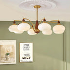 This Clérachic chandelier with eight white glass shades hangs against a sage green wall, above two framed posters.