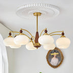A white glass Clérachic chandelier hangs below a ceiling rose, with an oval framed portrait on the wall behind.