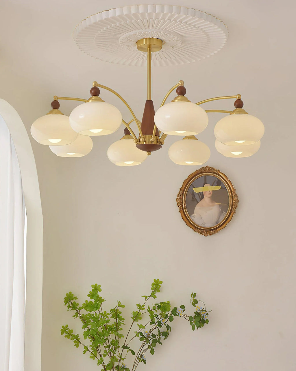 Eight white glass shades on this Clérachic chandelier, hung under a pleated ceiling rose beside an oval portrait.
