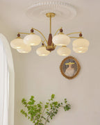 Eight white glass shades on this Clérachic chandelier, hung under a pleated ceiling rose beside an oval portrait.