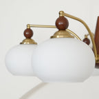 Close view of two white glass shades, with gold caps and wooden finials, on this Clérachic chandelier.