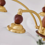 Close view of a gold cap, a round wooden finial and the curved arm above a white glass shade on this Clérachic chandelier.