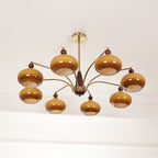 This Clérachic chandelier with brown glass shades on curved gold arms, switched off, hung below a white ceiling.