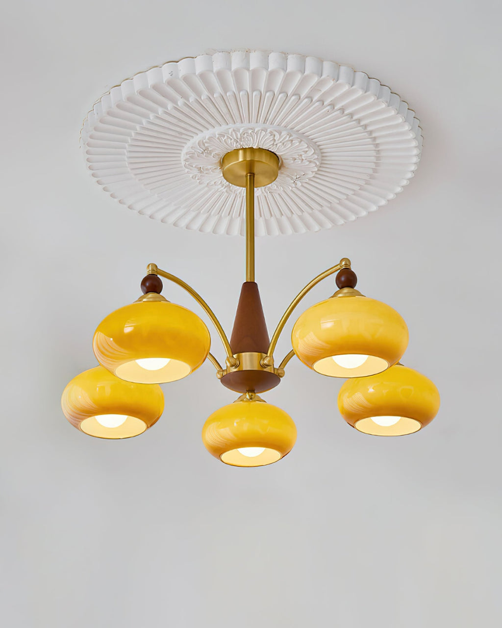 A caramel glass Clérachic chandelier lit under a pleated white ceiling rose, with five shades on gold arms.