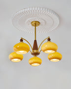 A caramel glass Clérachic chandelier lit under a pleated white ceiling rose, with five shades on gold arms.