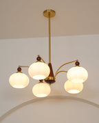 Five white glass shades glowing warm on this Clérachic chandelier, with a gold rod and ceiling plate and a curved arch behind.