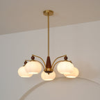 This Clérachic chandelier, lit with five white glass shades, hangs from a long gold rod in front of a curved arch.