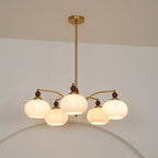 A Clérachic chandelier with five lit white glass shades seen from slightly below, with a gold ceiling plate above.