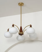 White glass Clérachic chandelier, unlit, with its shades pointing down on curved gold arms against a pale wall.