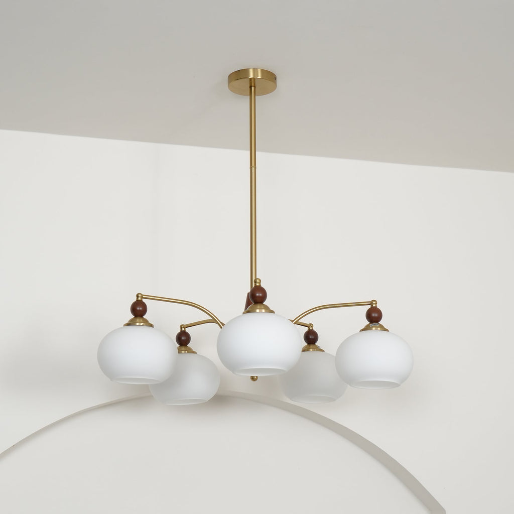 Side view of the unlit white glass Clérachic chandelier, hanging from a gold rod below a white ceiling.