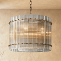 Clérachic compact drum chandelier of clear fluted glass rods with antiqued brass studs on a chain, glowing against warm plaster.