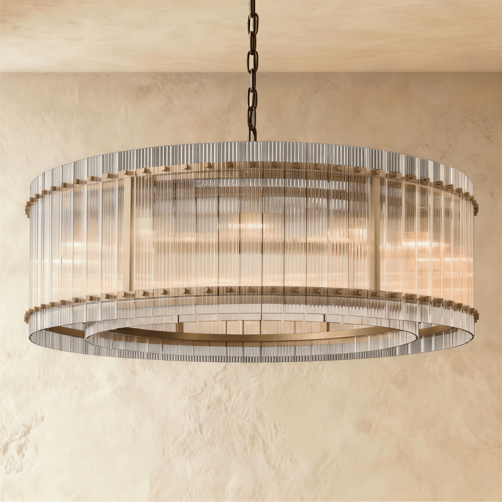 Clérachic larger drum chandelier of fluted glass rods with antiqued brass studs and an inner ring, lit warm on a chain.