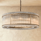 Clérachic larger drum chandelier of fluted glass rods with antiqued brass studs and an inner ring, lit warm on a chain.