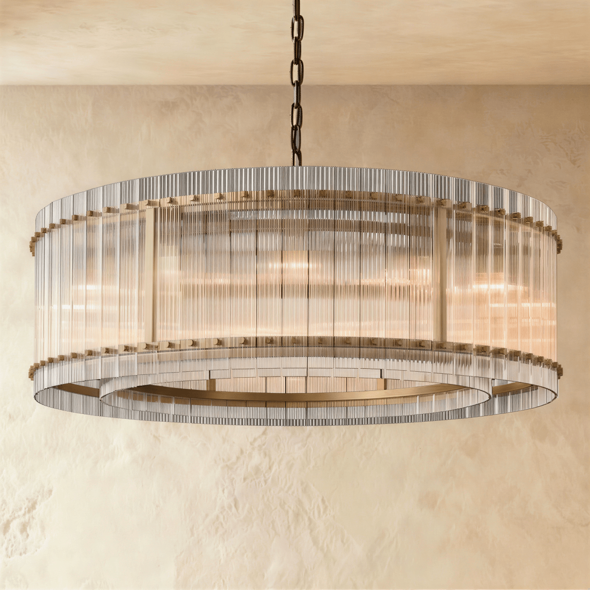 Clérachic larger drum chandelier of fluted glass rods with antiqued brass studs and an inner ring, lit warm on a chain.