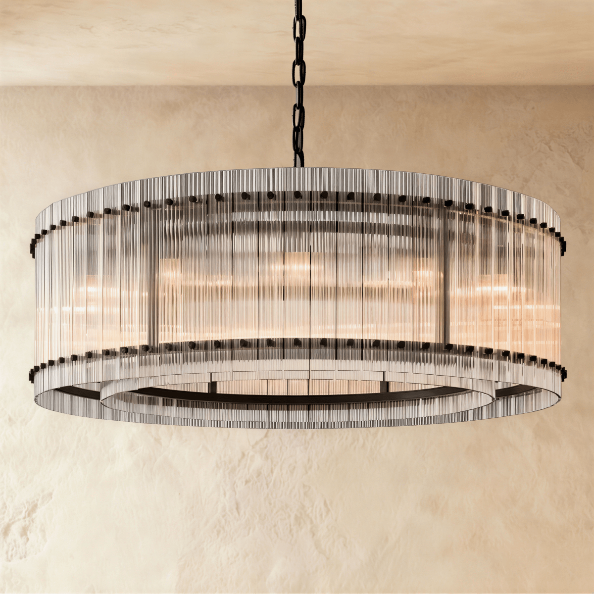 Clérachic larger drum chandelier of fluted glass rods with matte black studs and an inner ring, lit warm on a chain.
