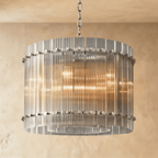 Clérachic compact drum chandelier of clear fluted glass rods with polished nickel studs on a chain, glowing against warm plaster.