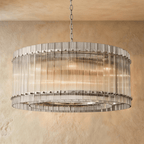 Clérachic wide drum chandelier of clear fluted glass rods with polished nickel studs, hung on a chain against warm plaster.