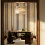 Clérachic fluted glass drum chandelier with brass studs hanging above a desk and green velvet chairs in a striped-wallpaper study.