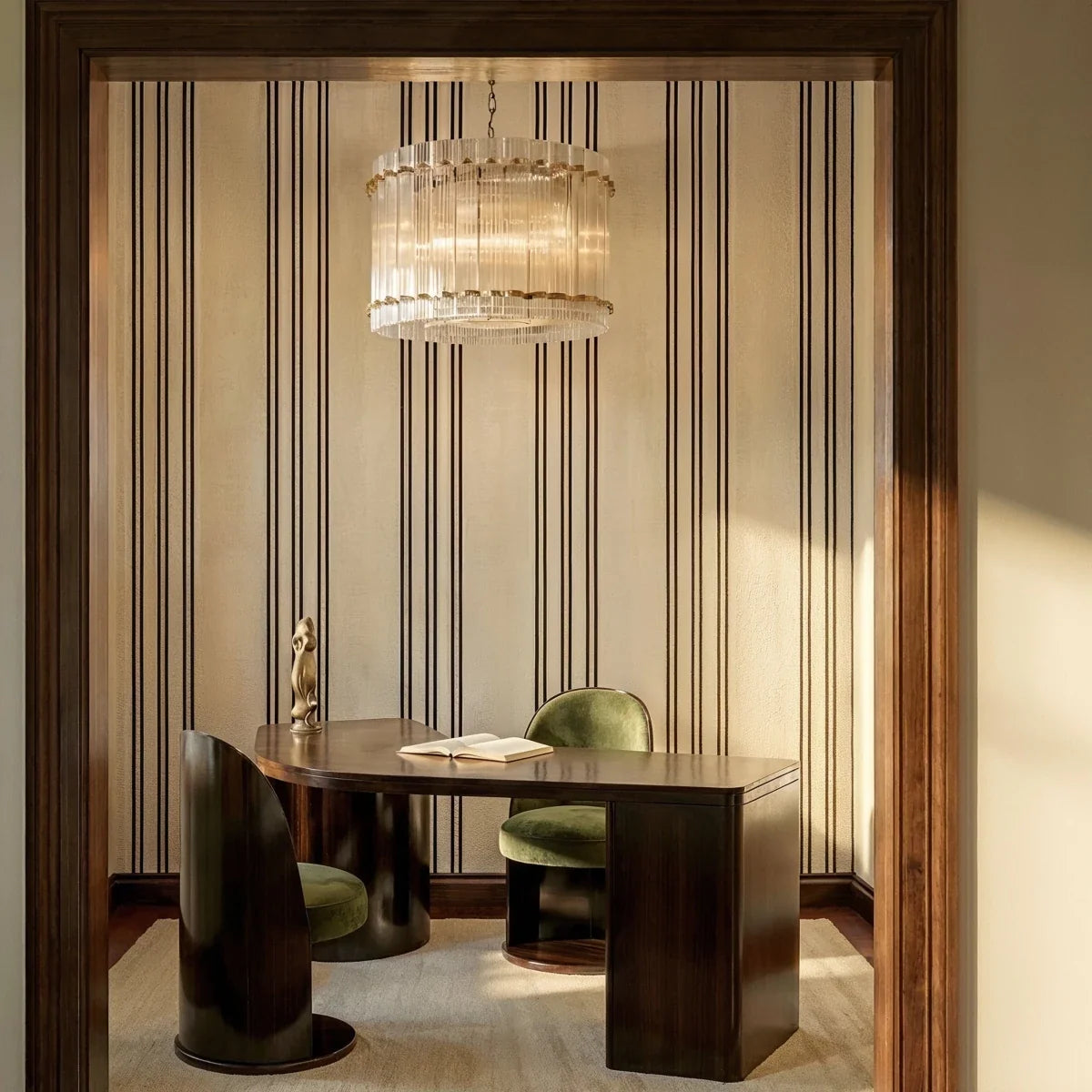 Clérachic fluted glass drum chandelier with brass studs hanging above a desk and green velvet chairs in a striped-wallpaper study.