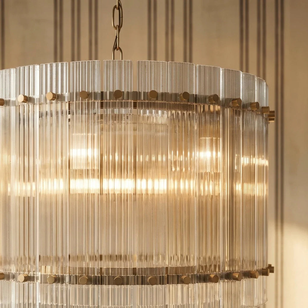Clérachic fluted glass drum chandelier close up, showing the brass studs and warm light glowing through the clear rods.