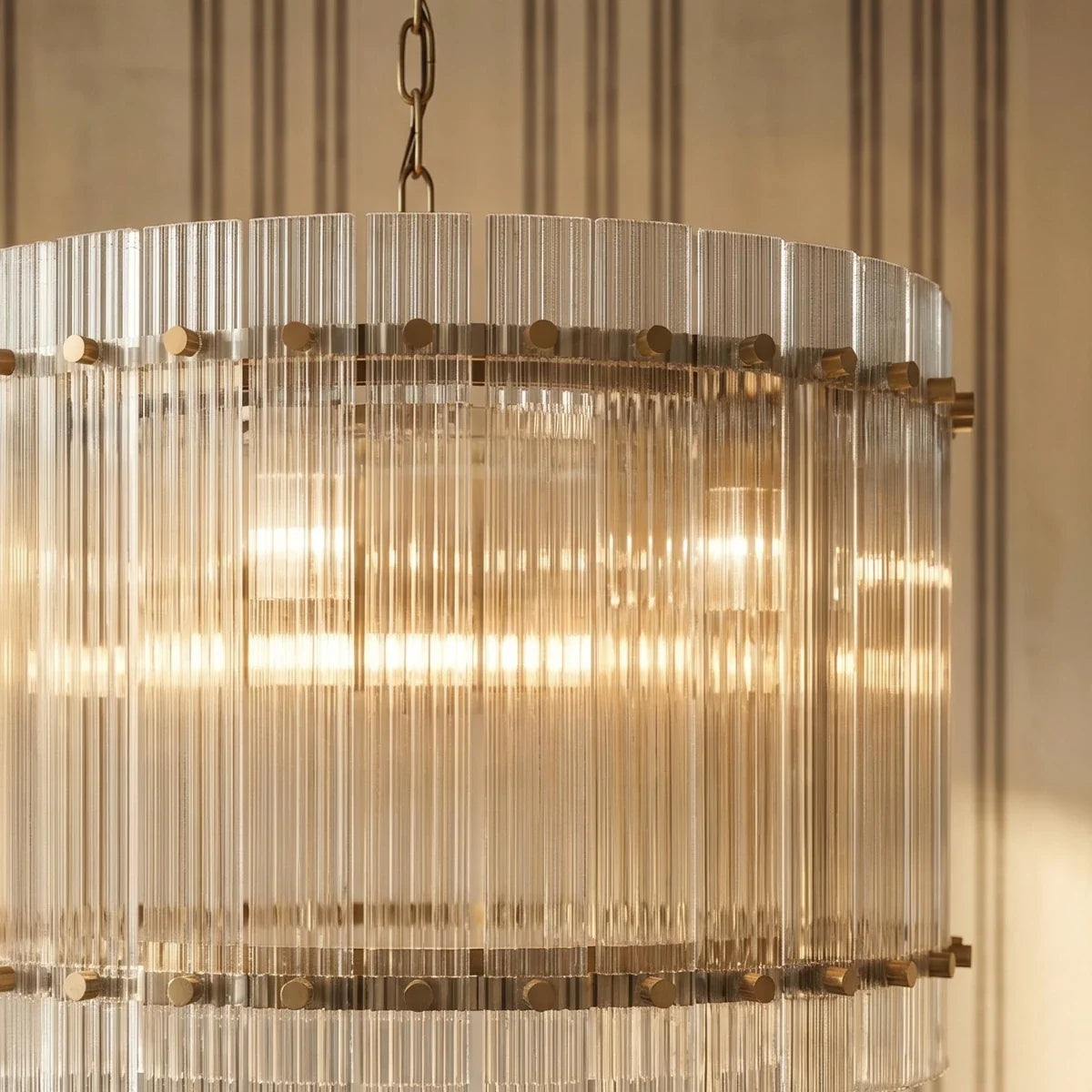 Clérachic fluted glass drum chandelier close up, showing the brass studs and warm light glowing through the clear rods.