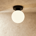 Clérachic flush-mount light in matte black, a single opal glass globe glowing warm on a plaster ceiling.