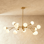 Clérachic branching chandelier in brushed gold, a wide dense spread of opal glass globes lit warm.