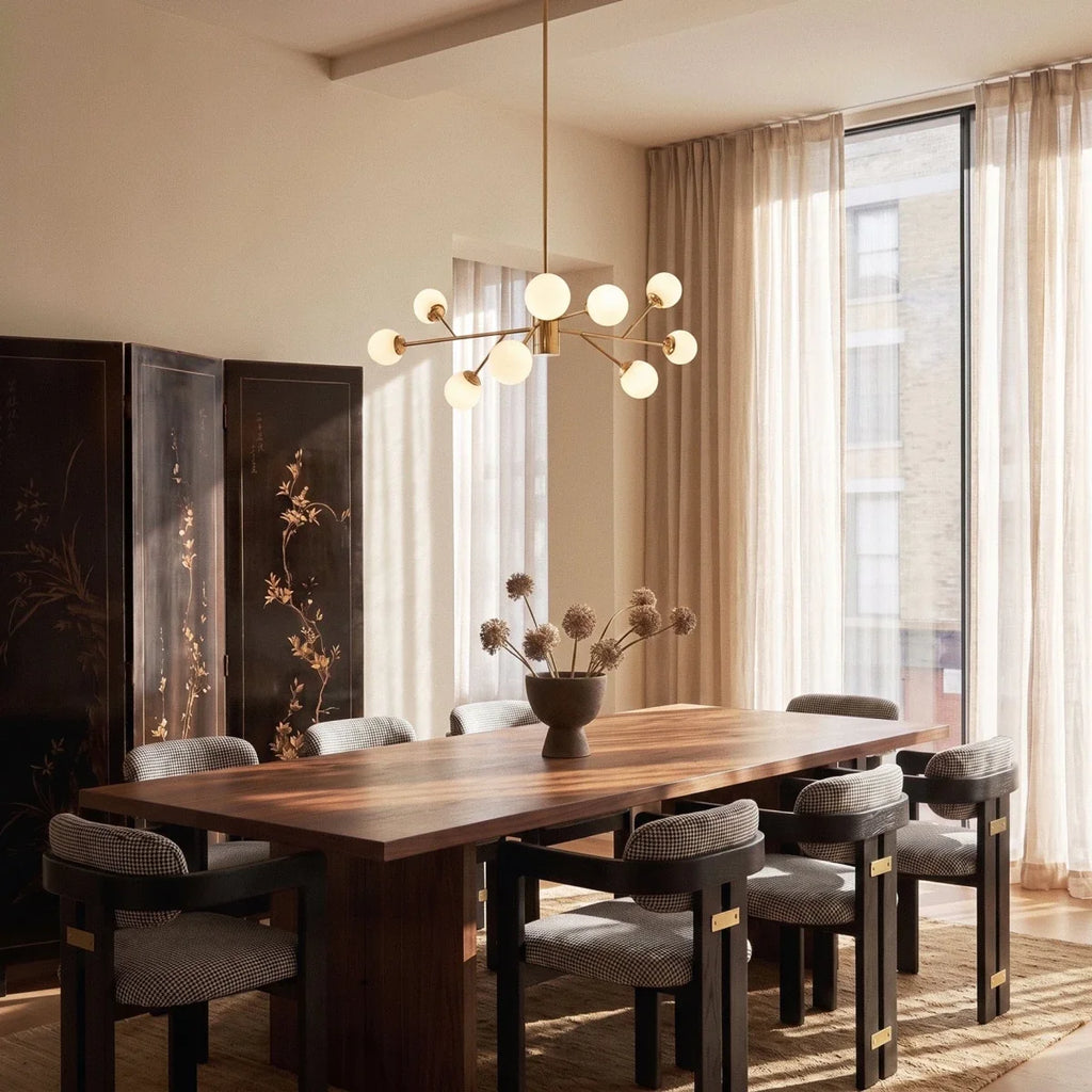 Clérachic branching chandelier in brushed gold lit warm above a walnut dining table set for eight.