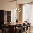 Clérachic branching chandelier in brushed gold lit warm above a walnut dining table set for eight.