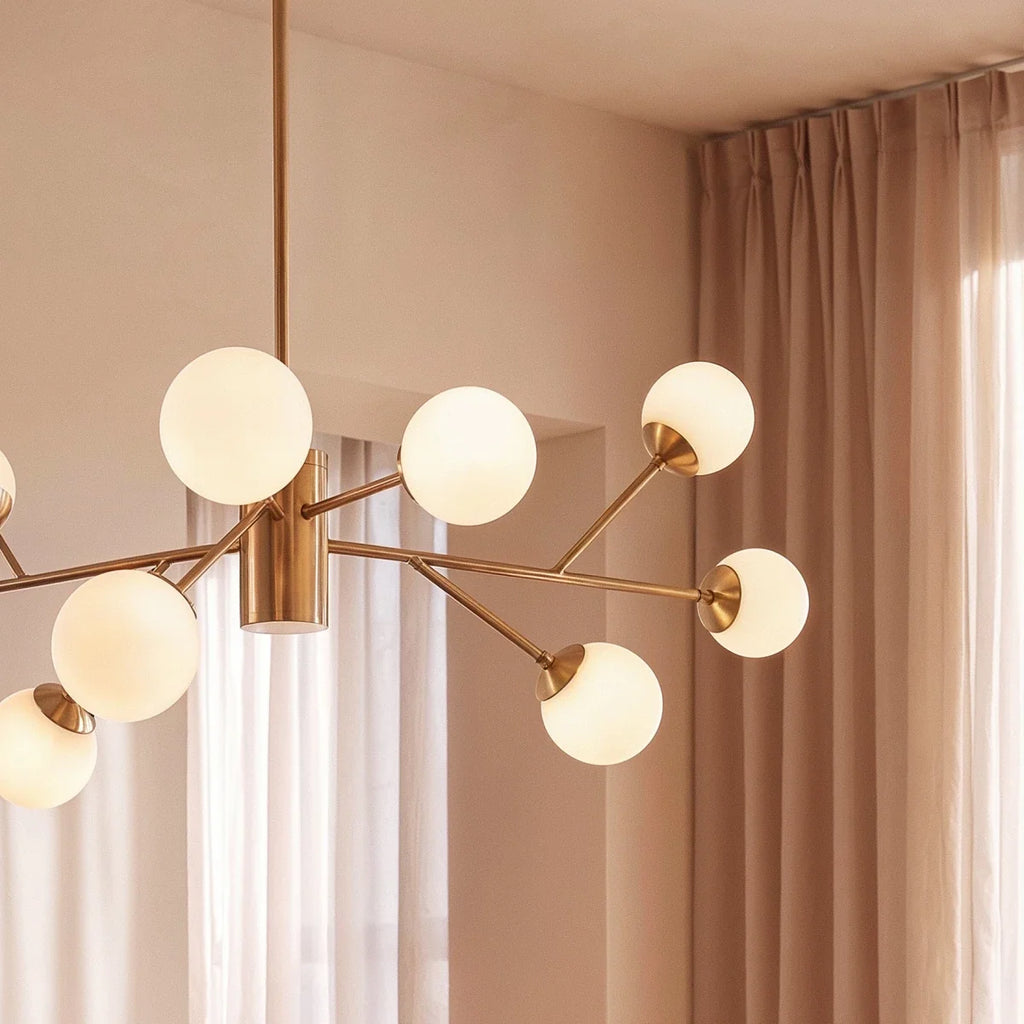 Clérachic branching chandelier detail in brushed gold, opal glass globes close against sheer curtains.