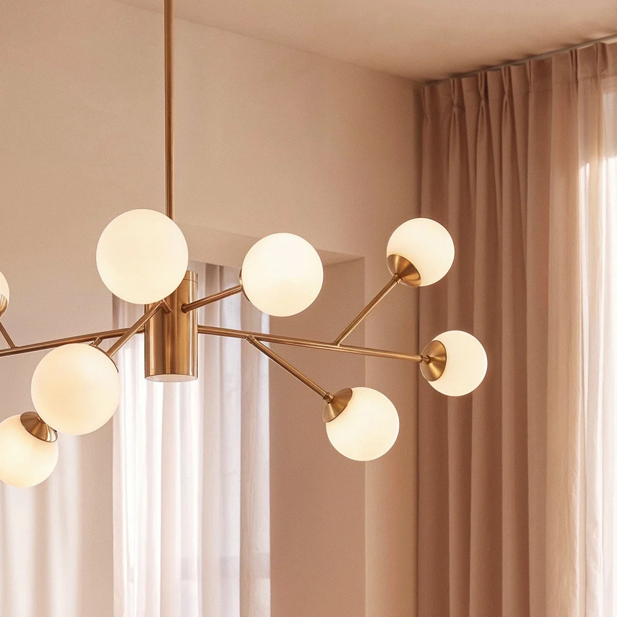 Clérachic branching chandelier detail in brushed gold, opal glass globes close against sheer curtains.