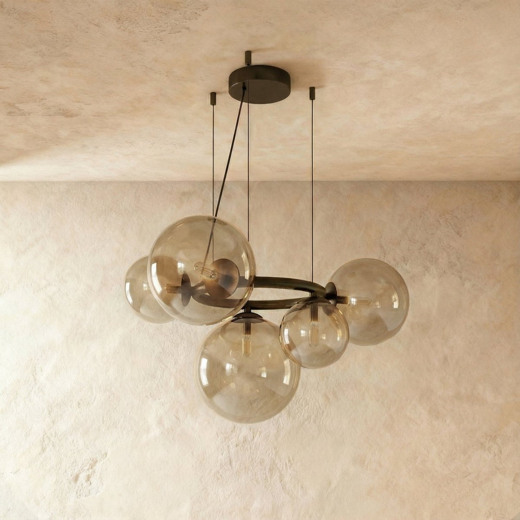 Clérachic globe cluster chandelier in Clear Glass, exposed warm bulbs glowing inside spheres on a dark ring.