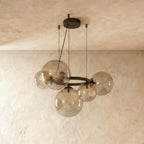 Clérachic globe cluster chandelier in Clear Glass, exposed warm bulbs glowing inside spheres on a dark ring.