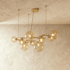 Clérachic globe cluster chandelier in Amber Glass, a larger cluster of warm-tinted spheres on brass, glowing softly.