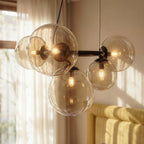 Close-up of the Clérachic globe cluster chandelier's Clear Glass spheres, warm bulbs glowing on a dark ring frame.